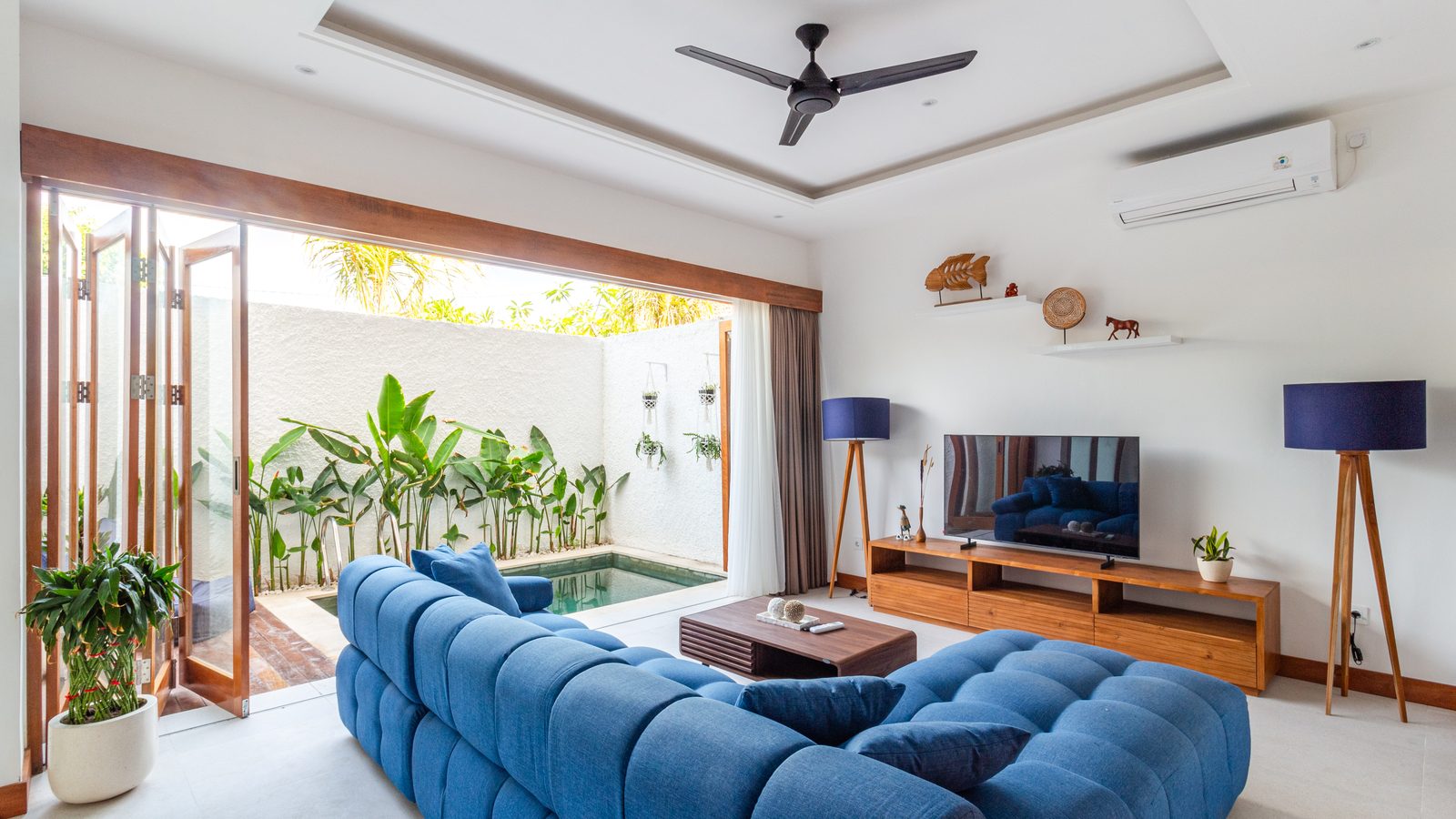 Wohnraum einer Villa mit blauem Sofa, offenen Faltfenstern und Pool im Innenhof